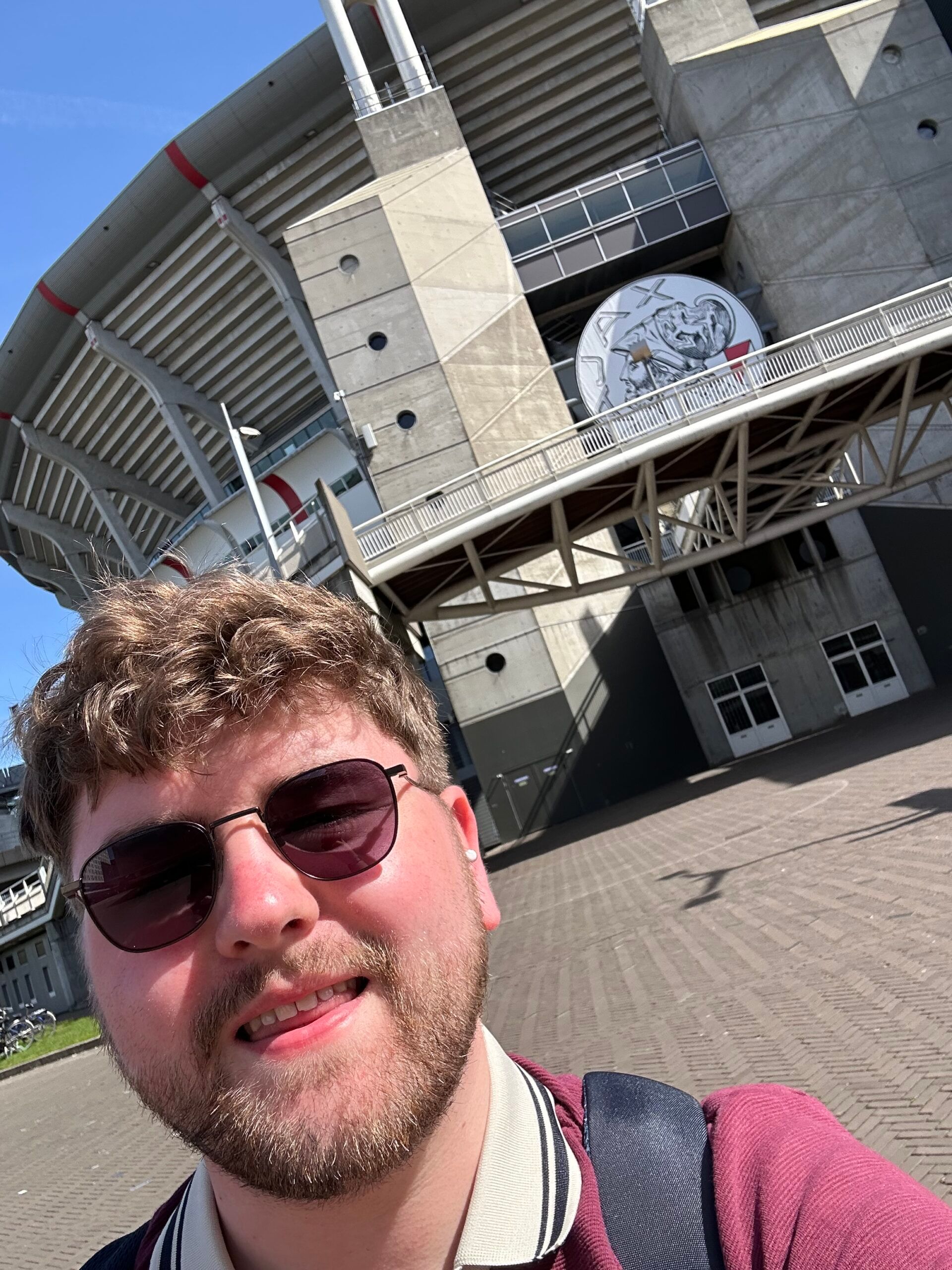 Selfie in front of a stadium, with a man wearing sunglasses and a maroon shirt in the foreground.