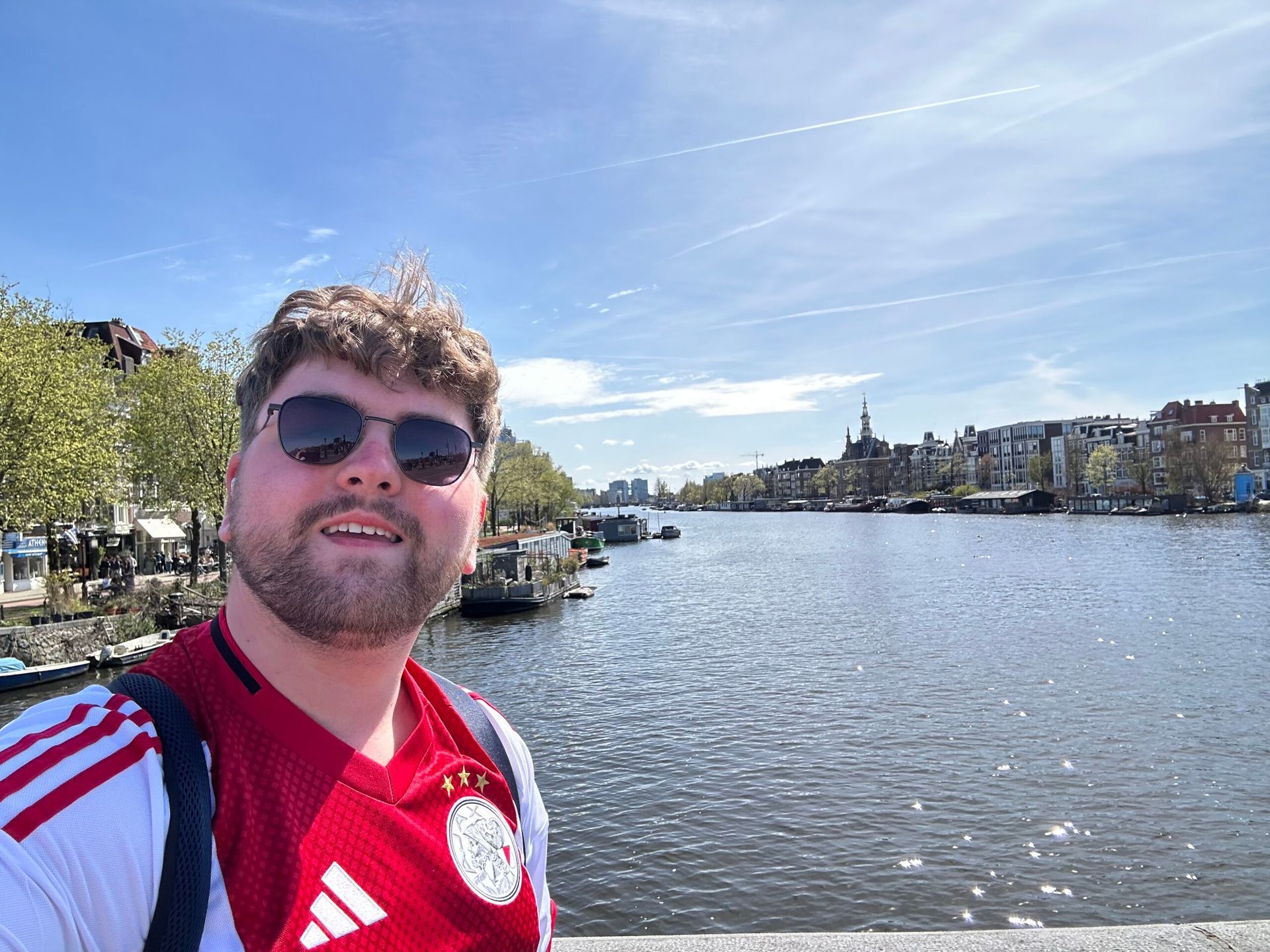 Selfie by a waterfront on a sunny day, with city buildings and blue sky in the background