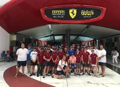 Group of students and adults posing outside a Ferrari-themed building entrance, with a red arch overhead