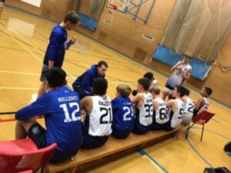 Basketball team in blue and white jerseys seated on a gym bench during a timeout