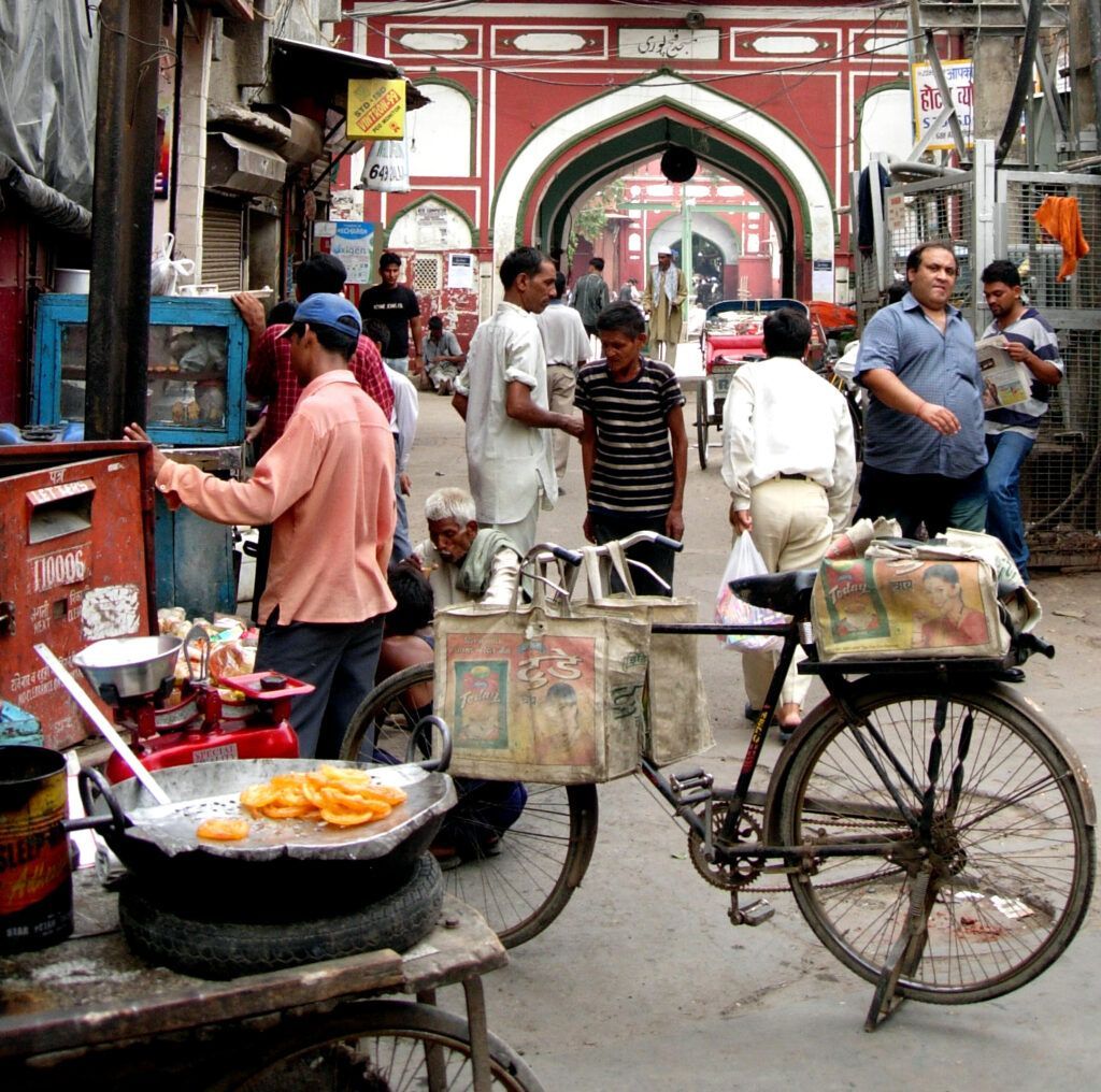 Bustling street market with bicycles, food stalls, and pedestrians near a red arched gate.