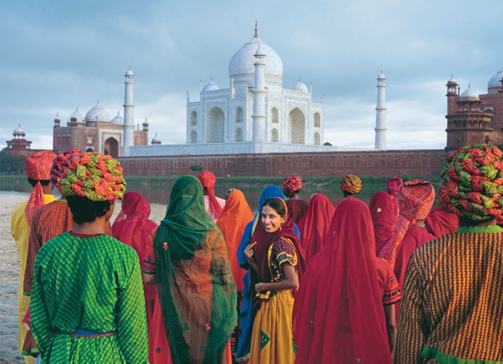 Women in colorful saris in front of the Taj Mahal with flower wreaths in their hair