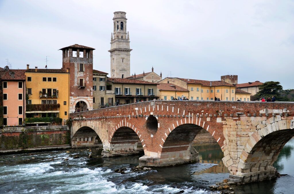 Stone bridge over a river with historic buildings and a tall tower in a European riverside town