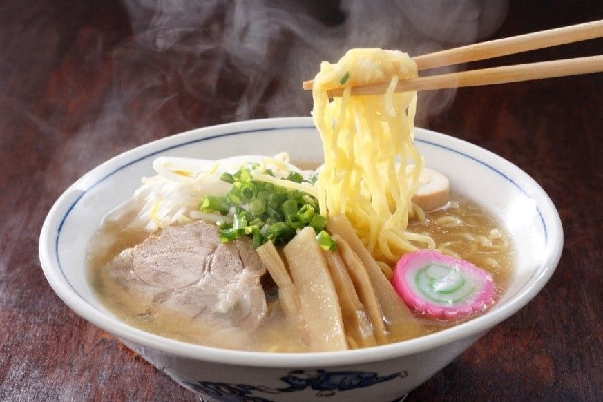 Steaming bowl of ramen with sliced pork, bamboo shoots, scallions, and noodles lifted by chopsticks