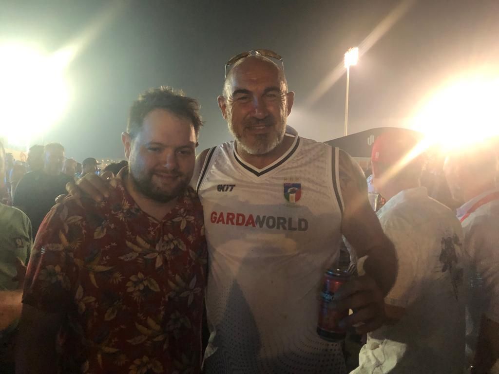 Two men posing at a nighttime outdoor event, one in a GardaWorld shirt holding a drink.