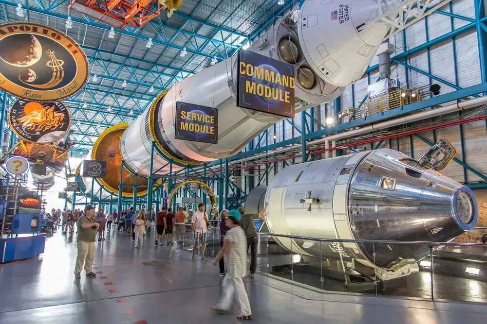 Astronaut exhibit with capsule and module in a bright museum hall, visitors walking below