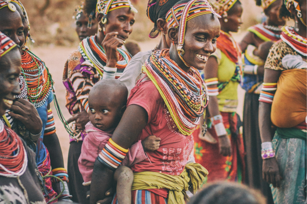 People in colorful beaded clothing and jewelry smiling together in an outdoor gathering