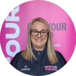 Smiling woman in glasses wearing a navy MSG Tours shirt against a pink branded backdrop