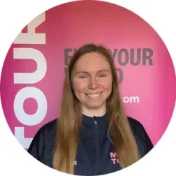 Smiling woman in navy jacket standing before a pink branded backdrop