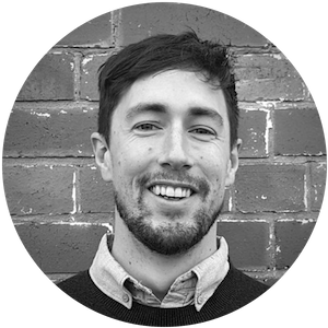 Smiling man with short dark hair and beard in front of a brick wall