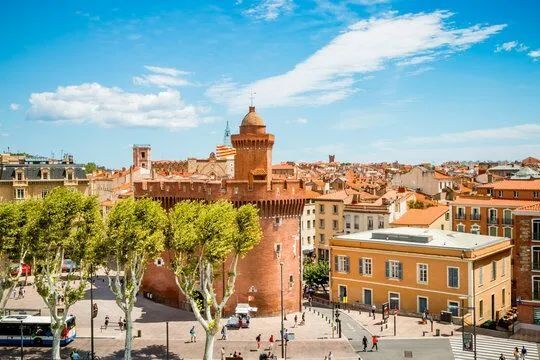 Sunny aerial view of a red-brick city gate and plaza with yellow buildings and trees under a blue sky