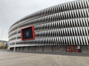 Modern stadium exterior with curved white facade and red-trimmed entrance panel