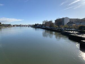 Calm river with marina and buildings along the right bank under a clear blue sky