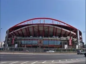 Large red-roofed stadium exterior on a sunny day, viewed from across a street.