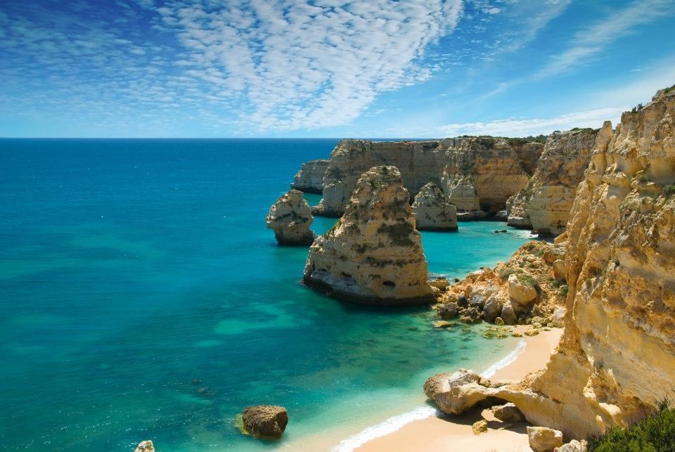 Turquoise sea and sandy cove beneath golden limestone cliffs under a bright blue sky