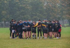 Soccer team huddled together on a grassy field in rainy weather