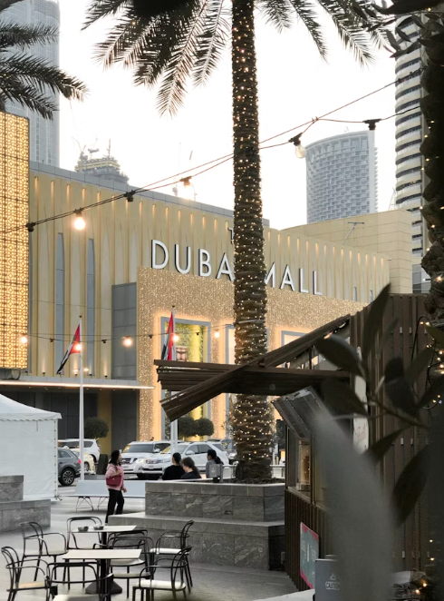 Outdoor Dubai Mall entrance at dusk with palm trees, lit facade, and café seating