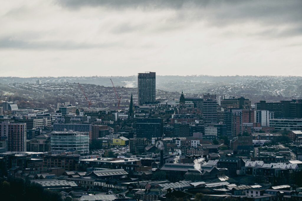 Wide city skyline under a cloudy sky, with a tall central tower and dense urban buildings.