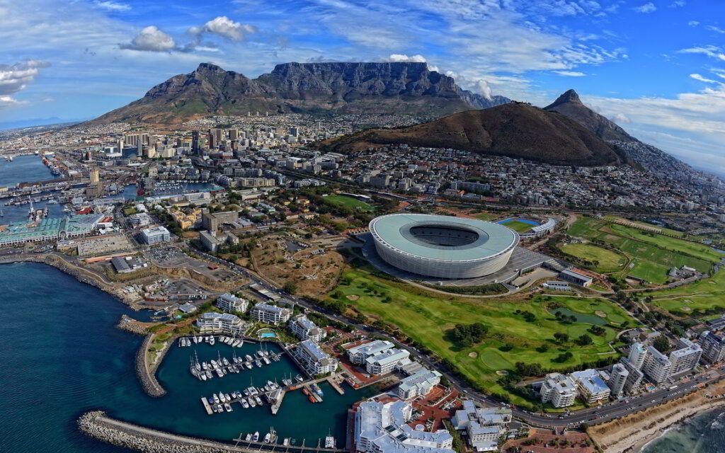 Aerial view of Cape Town with Table Mountain, city, harbor, and the circular Green Point Stadium by the coast