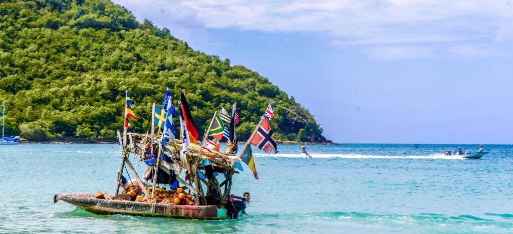 Colorful boat with flags on turquoise water near a lush green island under a blue sky