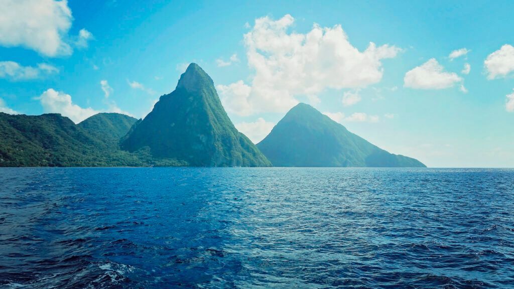 Tropical island with steep green mountains rising from a blue ocean under a partly cloudy sky
