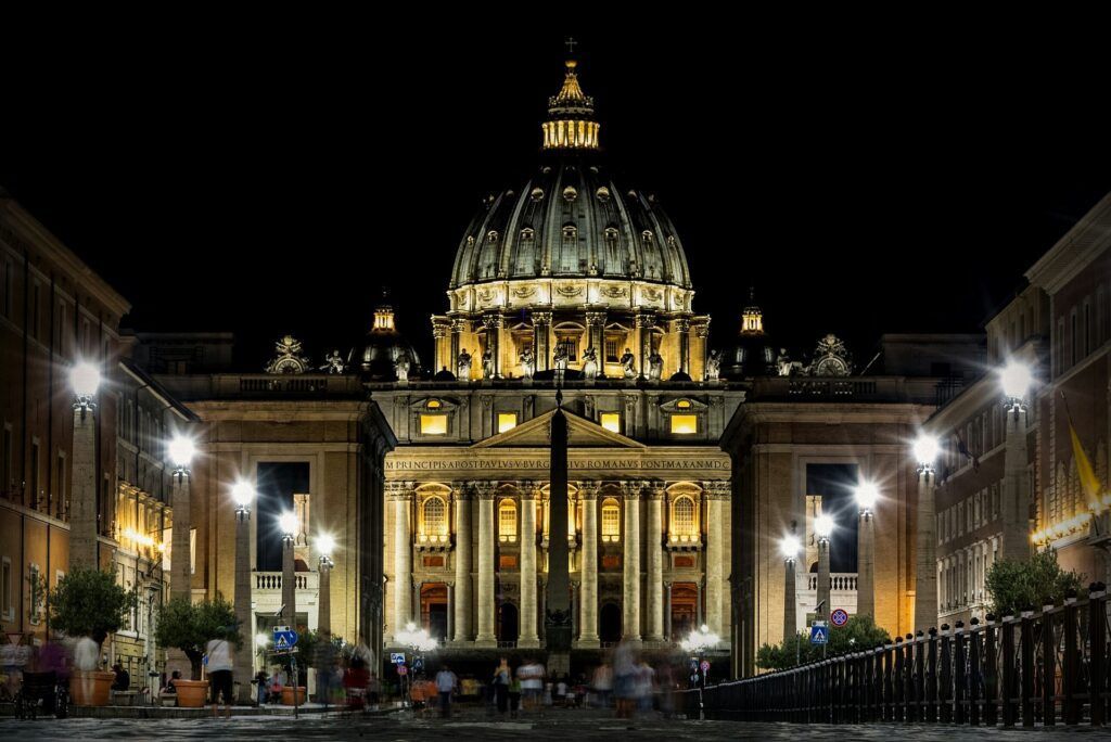 St. Peter’s Basilica illuminated at night, with a lit dome and a symmetrical colonnade in front.