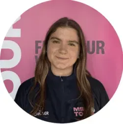 Portrait of a smiling person in a navy shirt before a pink branded backdrop