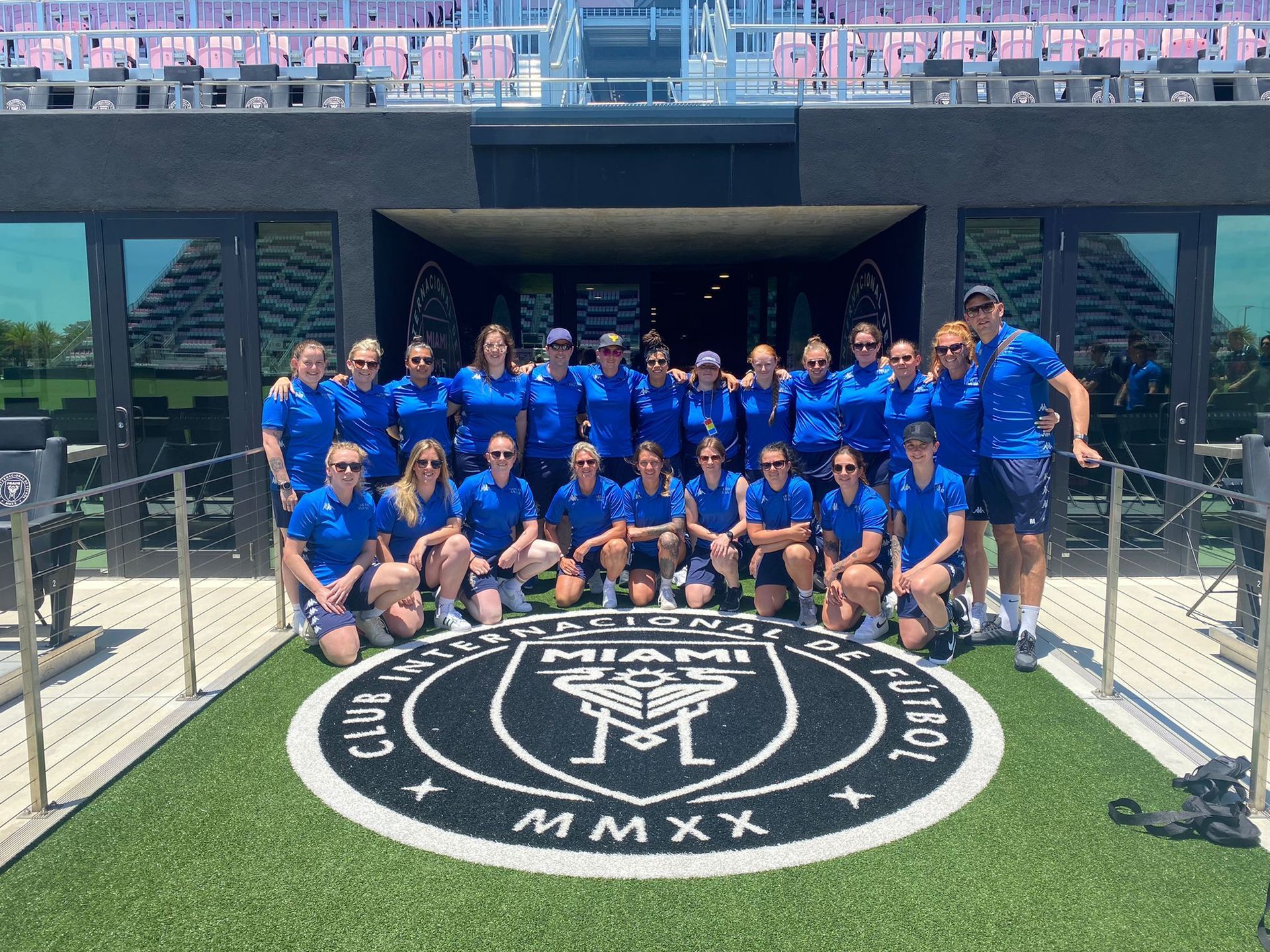 Group of soccer players in blue jerseys posing on a stadium walkway in front of a large circular club emblem