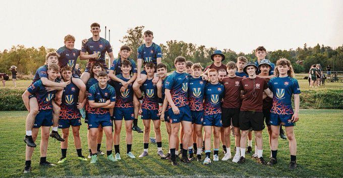 Youth sports team posing on a grassy field, wearing blue and maroon jerseys at sunset.
