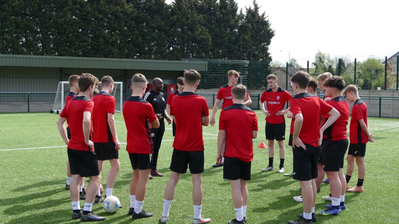 Group of players in red sports jerseys huddling on a soccer field during practice
