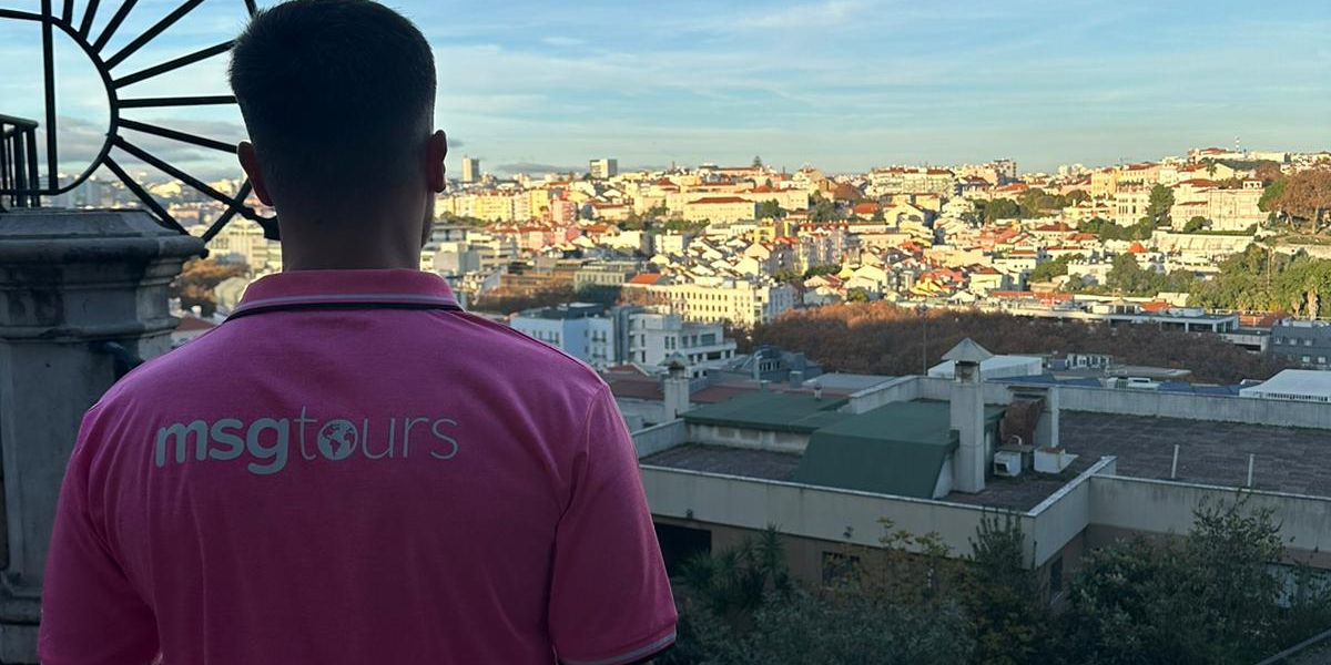 Person in a pink shirt overlooking a sunlit cityscape from a rooftop terrace