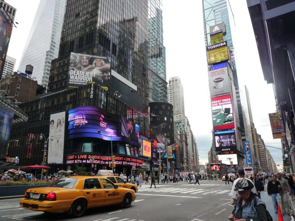 Busy Times Square street with yellow taxi, pedestrians, and tall LED billboards among skyscrapers