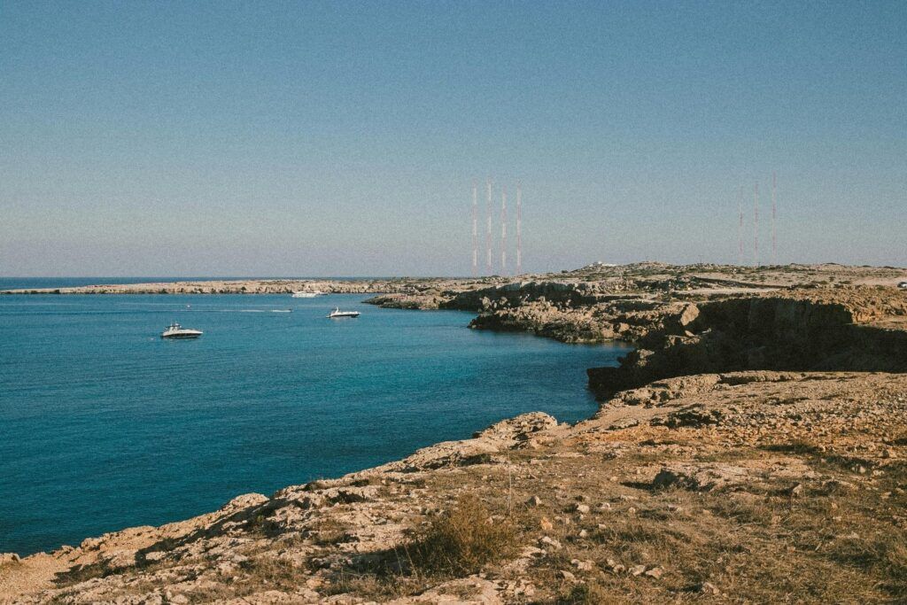 Rocky coastline overlooking a calm blue sea with a small boat in the distance under a clear sky