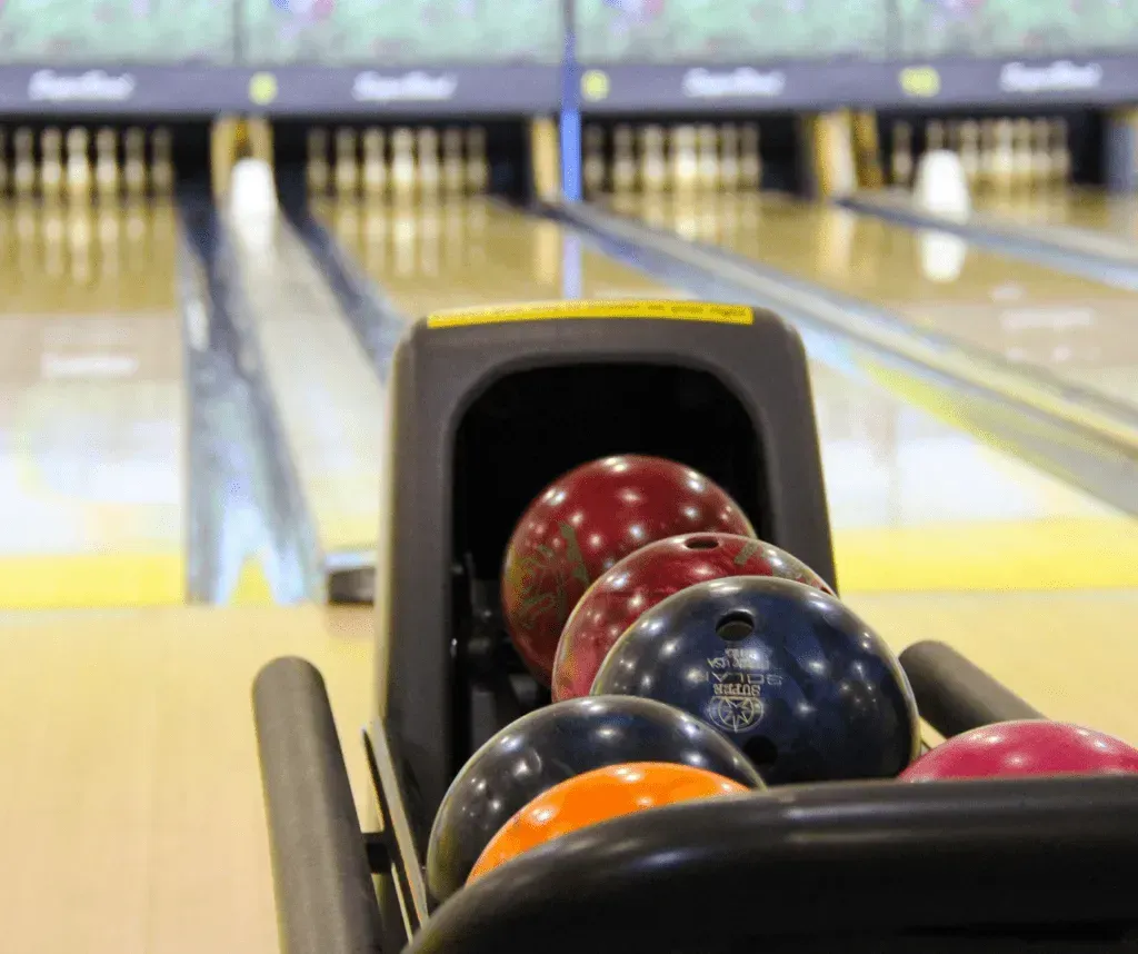 Bowling balls lined up in a return rack, with lanes stretching into the background.