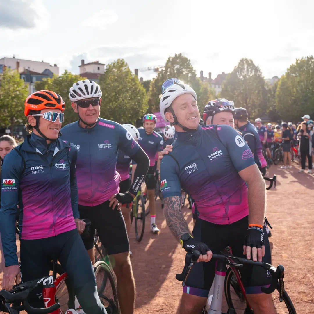 Cyclists in matching navy and pink jerseys posing together on a sunny road during a race event