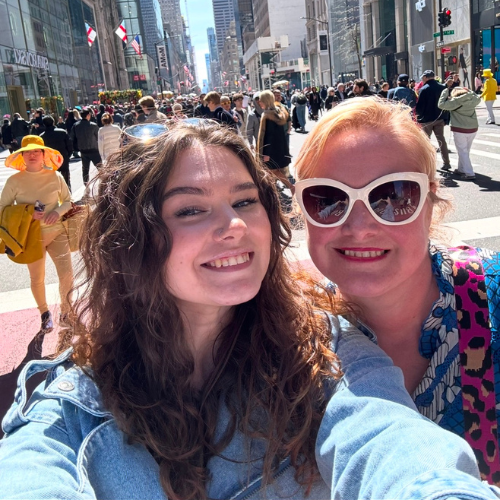 Two smiling people taking a selfie on a busy city street in bright daylight