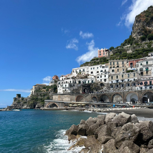 Colorful cliffside seaside village above turquoise water with rocky shoreline and blue sky
