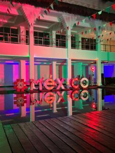 Colorful illuminated “MEXICO” sign in a glass-fronted venue with pink, purple, and green lighting