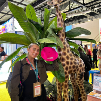 Woman posing beside a large giraffe statue at an indoor event booth
