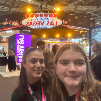 Two smiling people posing inside a Las Vegas casino under a glowing “Las Vegas” sign