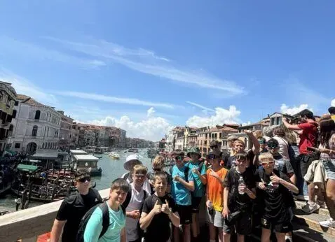 Crowd of people posing by a canal in a sunny city with historic buildings and blue sky