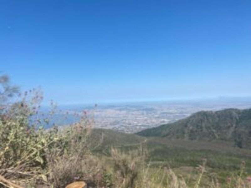 Mountains and green hills overlooking a distant coastal city under a clear blue sky