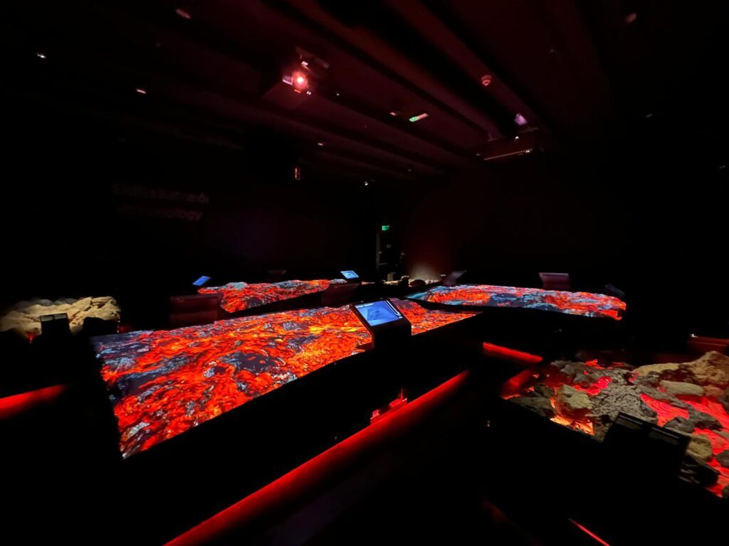 Dark room with glowing red-orange panels and beams of light on a stage-like floor