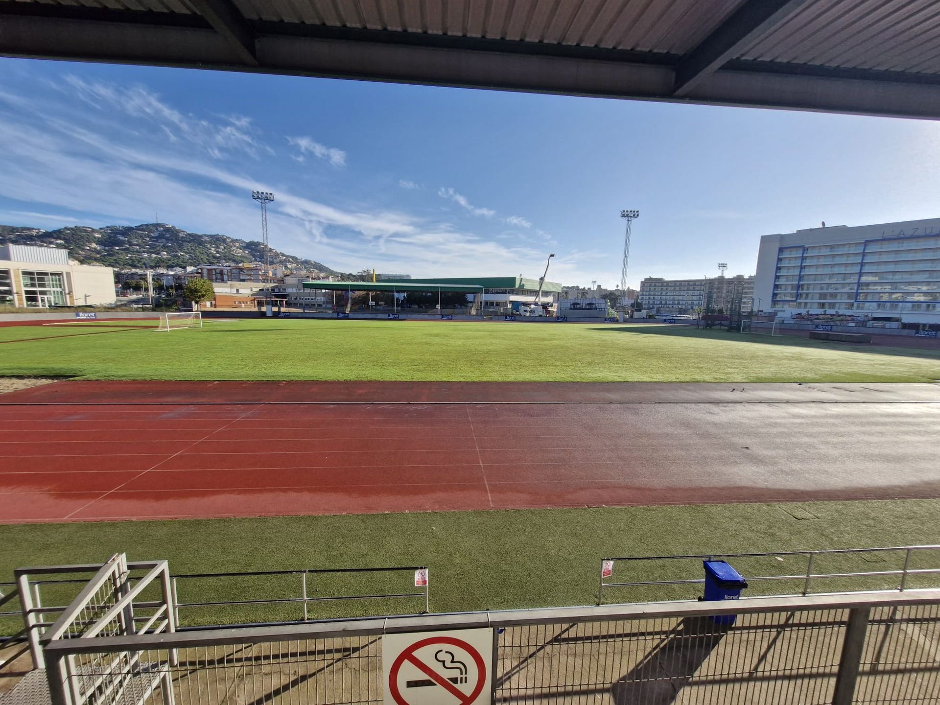 Empty sports field with red running track, viewed from under a stadium roof on a clear day