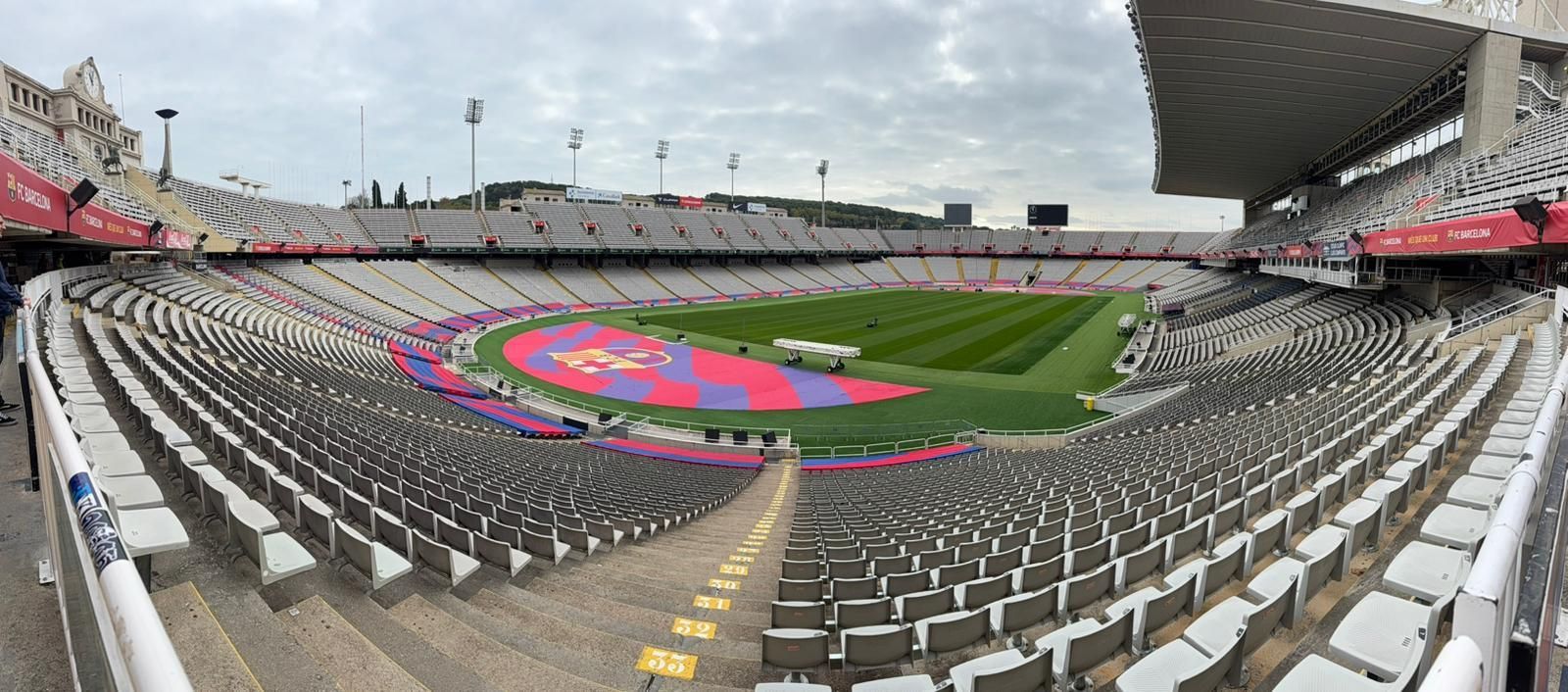 Wide-angle view of a mostly empty stadium with a colorful track field and covered stands under cloudy skies