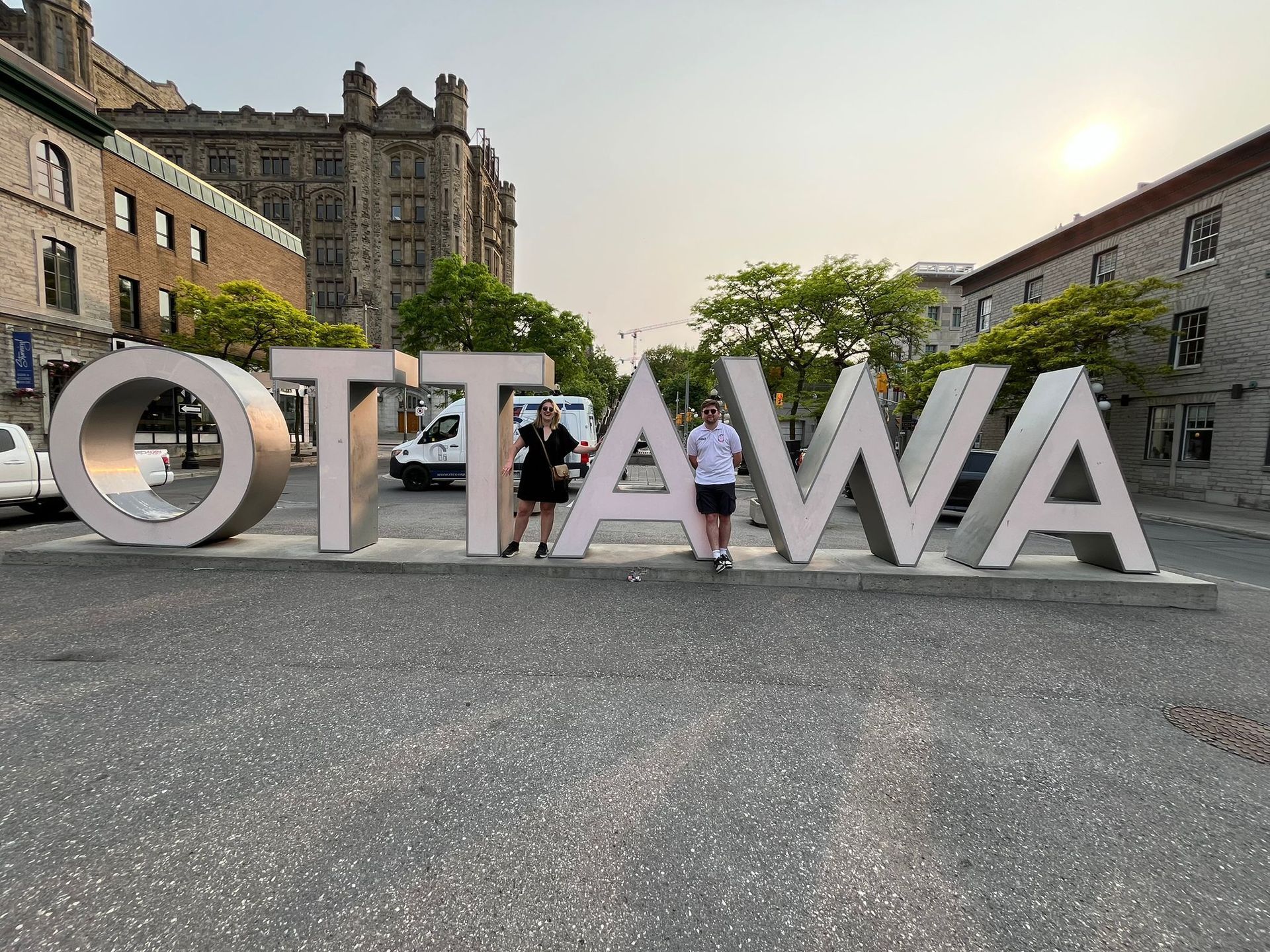 Large “OTTAWA” letters in a city plaza with people standing behind them at dusk.