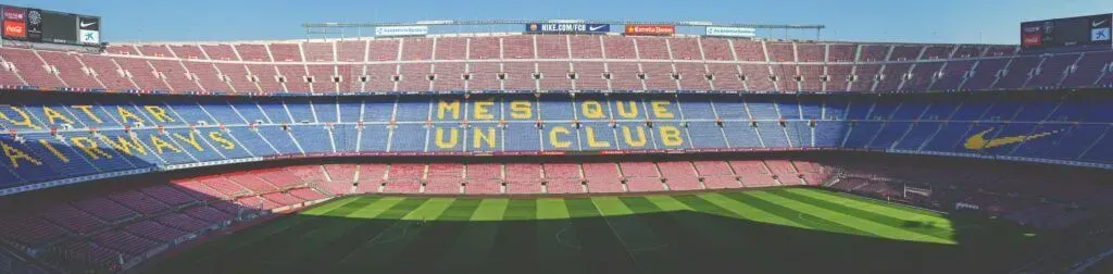 Empty football stadium with blue and red seats and a green pitch under sunlight