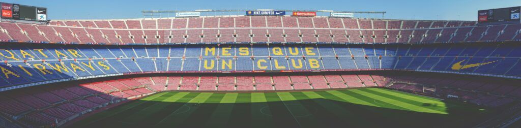 Wide view of a soccer stadium with red seats, green pitch, and “MÉS QUE UN CLUB” on the stands