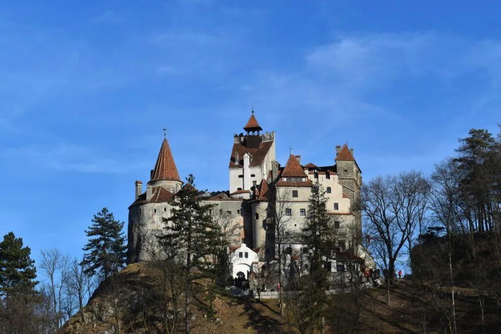 Hilltop castle with red-roofed towers against a blue sky and bare trees