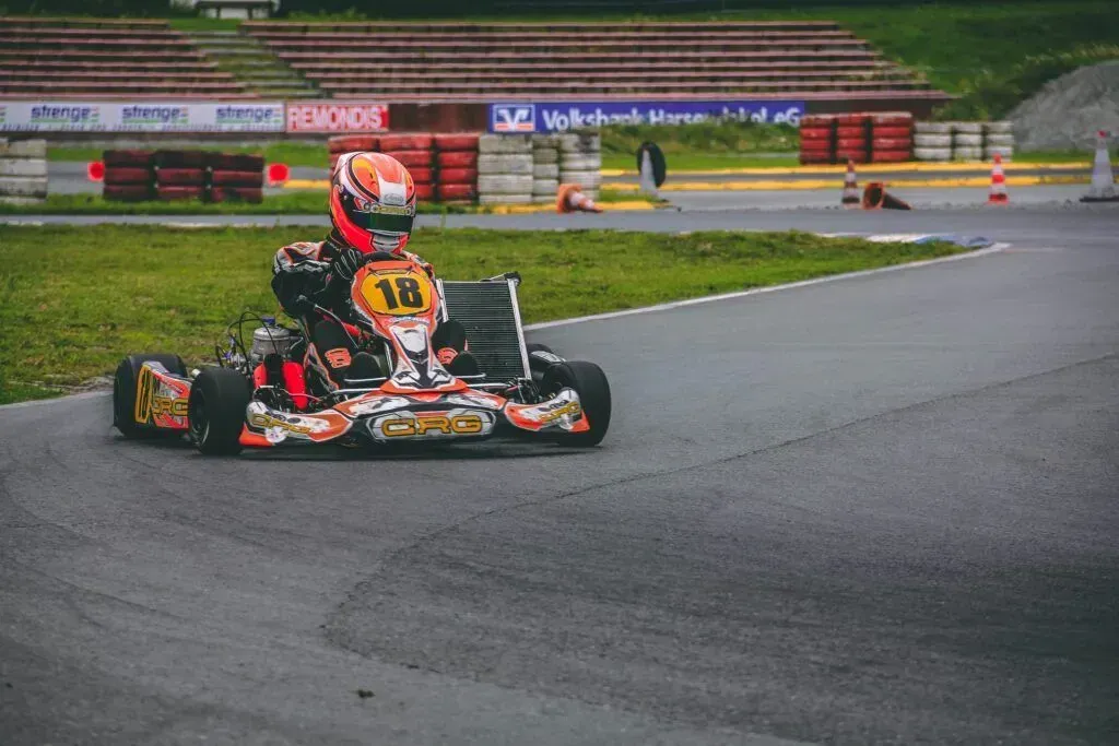 Kart racing on a wet track with a driver in orange and black turning a corner